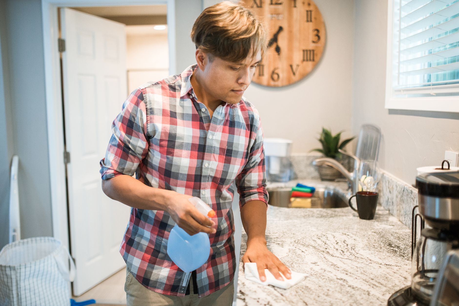 Asian man wiping kitchen counter using a cleaning solution in modern kitchen setting